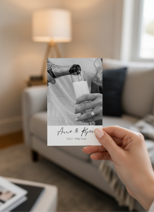 Hand holding a photo card with a black and white image of a couple and text in a living room.