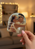 Hand holding a 'Save the Date' card with a couple kissing, blurred lights in the background