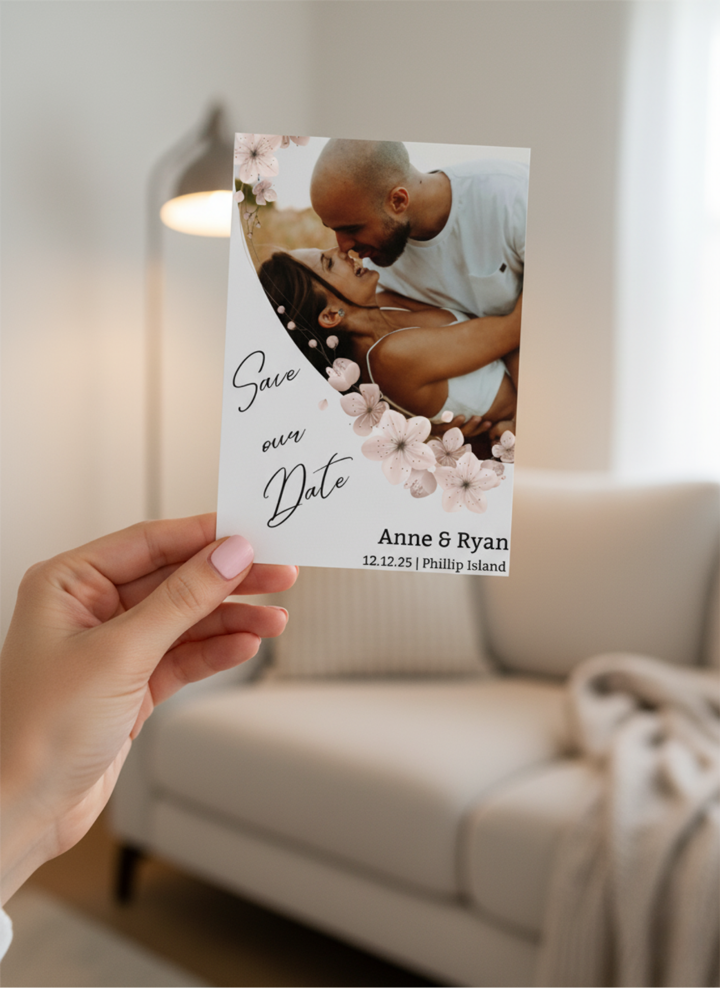 Hand holding a 'Save the Date' card with a couple's photo and text in a cozy living room.